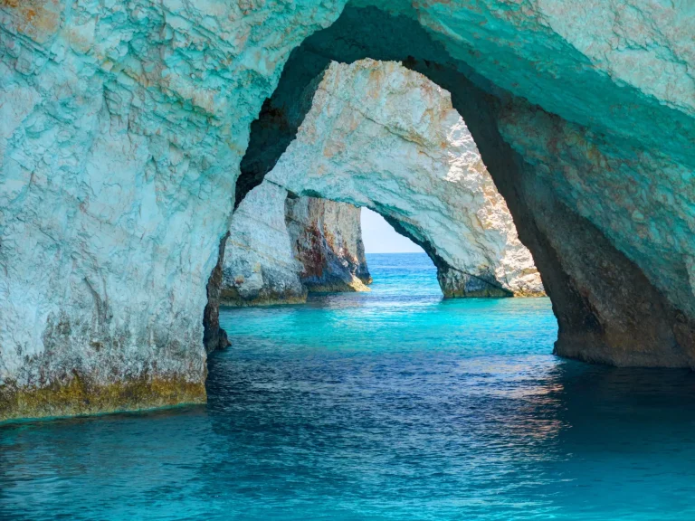 Beautiful view on Blue Caves rock arches from sightseeing boat with tourists in blue water of Ionian Sea inside Blue cave. Island Zakynthos Greece holidays vacation trips tours.